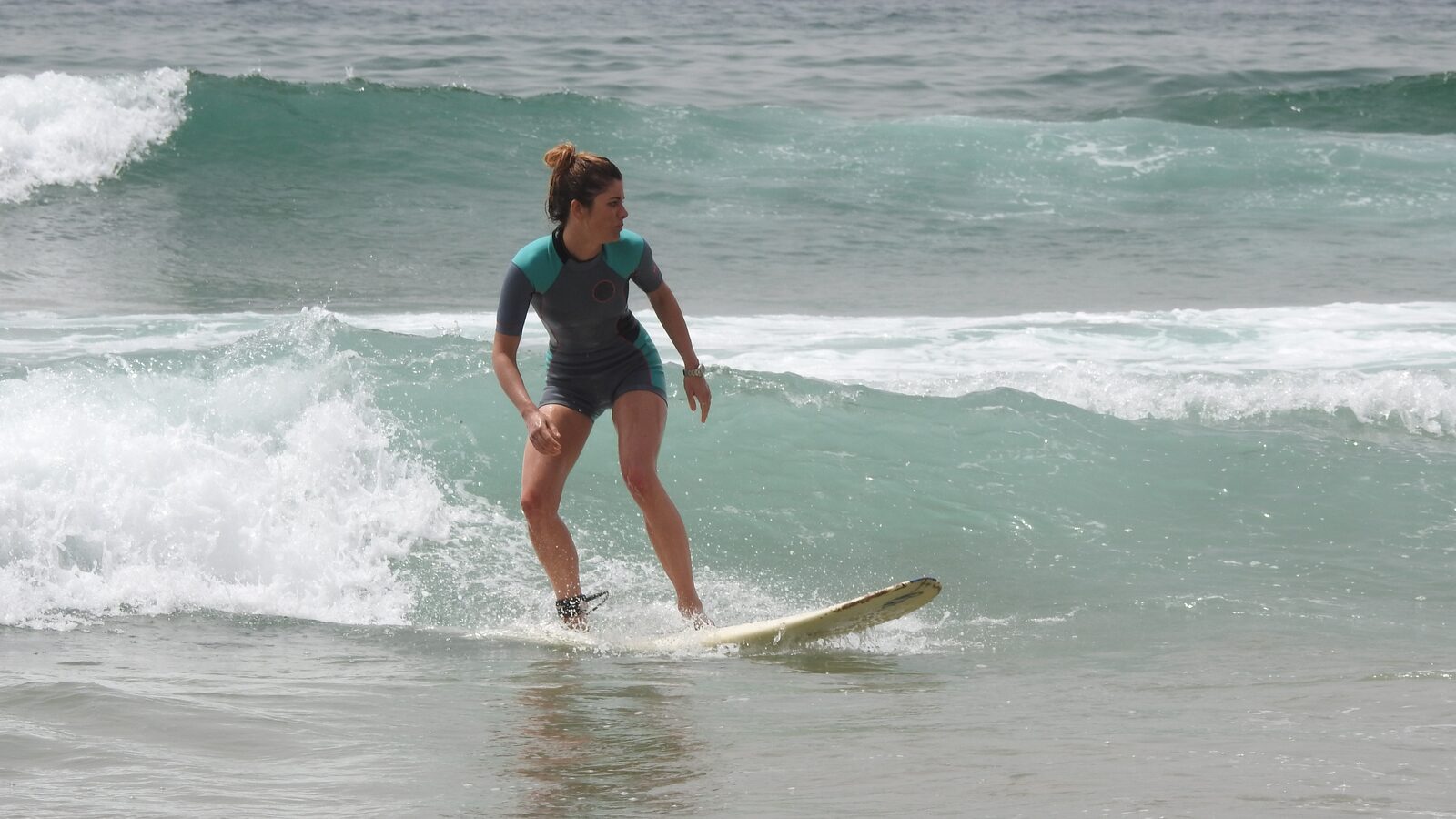 Beginner female surfer riding her wave in Agadir, stable stance in a shorty wetsuit, during a women's surf lesson.